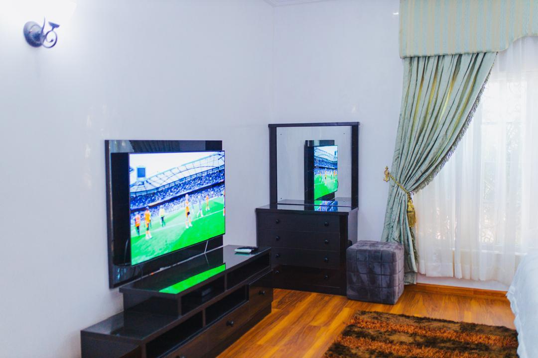 Bedroom with wall-mounted TV, dresser and wooden floor